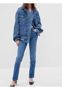 Blå denimjacka med oversized passform, två framfickor och silverknappar, kombinerad med slim fit blå jeans och svarta klackar.