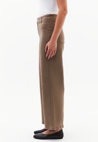 Ruske, høyt livs vide bukser laget av myk stoff, med lommer og knappelukking, kombinert med svarte flate sko.