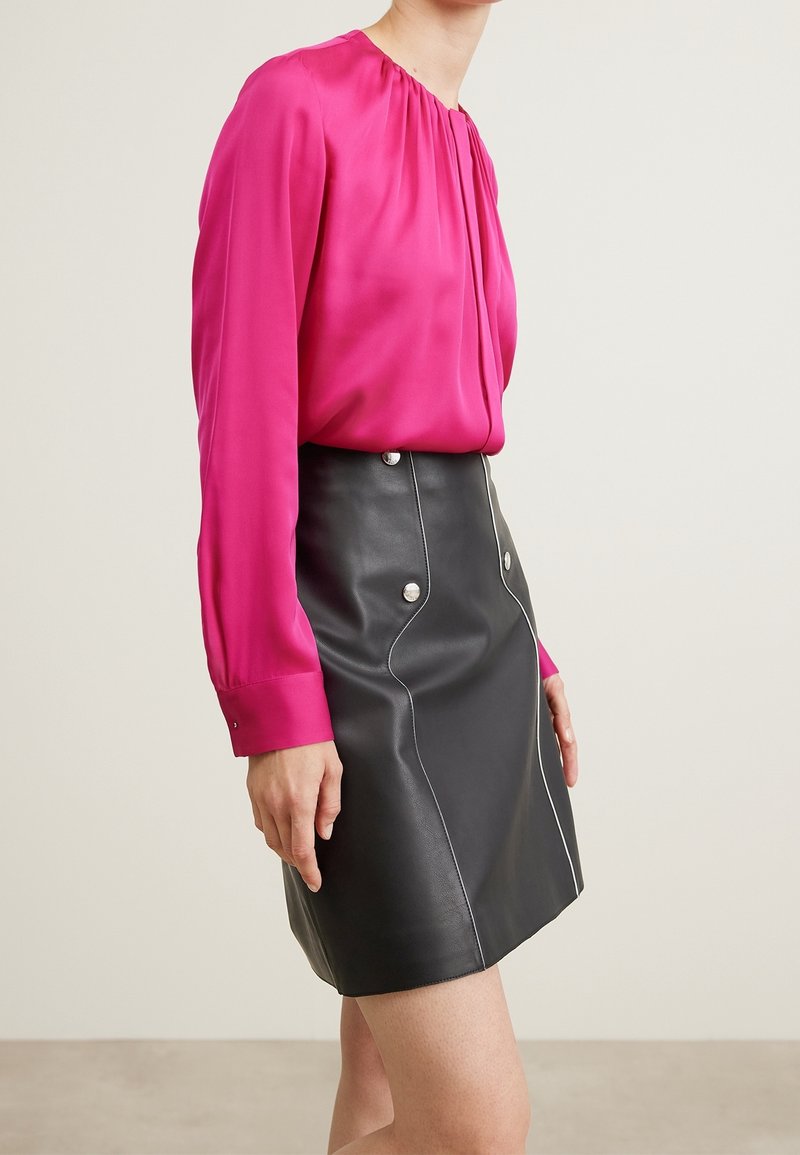 Fuchsia Satinbluse mit langen Ärmeln und gerafftem Kragen; schwarze Leder-Minirock mit silbernen Knöpfen und weißen Nähdetails.