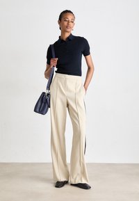 Polo shirt in tono navy con texture, pantaloni beige a vita alta a gamba larga con strisce laterali, ballerine nere e una piccola borsa a tracolla navy.