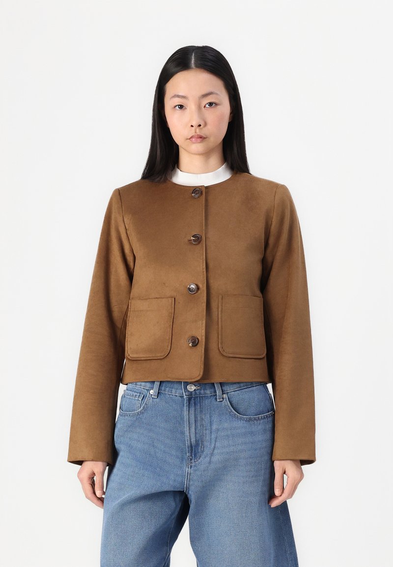 Brun cropped jakke med to frontlommer, knaplukning og en glat tekstur. Sammen med blå denimjeans.