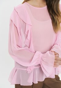 Helles pinkes Chiffon-Oberteil mit Rüschärmeln und Peplum-Saum. Halbdurchsichtiger Stoff mit elastischen Bündchen und subtiler Glanz, der eine zarte Textur zur Schau stellt.