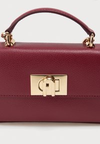 Bolsa de mão de couro texturizado em bordô, com um fecho de hardware dourado, formato estruturado e uma pega superior para transporte.