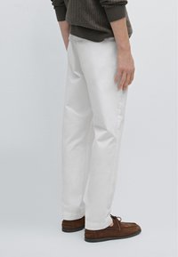 Witte katoenen broek met een getailleerde pasvorm, gecombineerd met bruine suède schoenen. De stof is soepel met een lichte glans; het ontwerp is strak en minimalistisch.