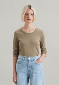 Long-sleeve, olive green top made of soft fabric, featuring a round neck and fitted sleeves, paired with light blue high-waisted jeans.