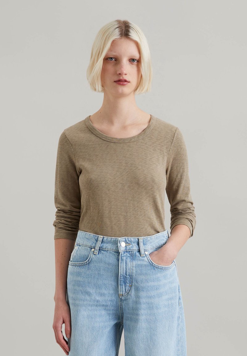 Long-sleeve, olive green top made of soft fabric, featuring a round neck and fitted sleeves, paired with light blue high-waisted jeans.