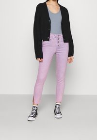 Svart ribbad cardigan, ljusgrå tanktop, rosa högmidjade skinny jeans och svarta högskor med vita sulor.