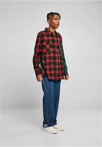 Rode en zwarte geruite flanellen shirt met groene accenten, voorzien van twee borstzakken, knoopsluiting aan de voorkant en lange mouwen. Draagt het met blauwe jeans en witte schoenen.