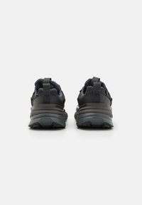 Melnas sporta kurpes ar teksturētu virsēju, mīkstu zoli un cilpiņām uz papēža, piedāvājot modernu, elegantu dizainu.