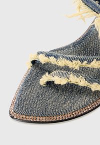 Denimsko med frynsete kanter og spiss tå, accentuert av en rad med rosa rhinestones langs den svarte sålen.