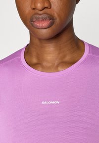 Μωβ αθλητική μπλούζα με υφή από πλέγμα και στρογγυλή λαιμόκοψη. Διαθέτει λευκό λογότυπο «SALOMON» στο στήθος.