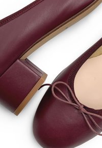 Ballerines en cuir bordeaux avec un bout arrondi, un talon plat et un nœud décoratif à l'avant. Surface texturée et bord élastiqué.