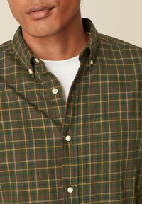 Groen geruit overhemd met knopen, met tinten geel, bordeauxrood en marineblauw, voorzien van een klassieke kraag en witte knopen op een zachte stof.