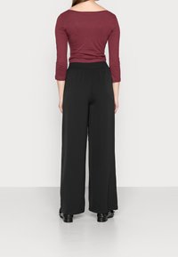 Bordová blůza s třičtvrtinovými rukávy v kombinaci s černými širokými nohavicemi. Hladký materiál, elastický pas a délka ke kotníkům zvyšují pohodlí.