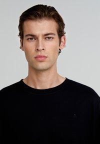 Sort crew-neck t-shirt lavet af bomuld. Har korte ærmer og en lille logo-accent på brystet. Glat tekstur og afslappet pasform.