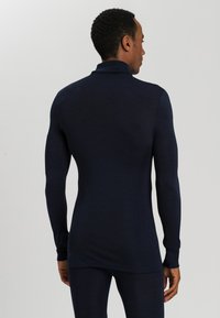 Maglietta termica a maniche lunghe navy con alto colletto, polsini a costine e una forma aderente. Realizzata in materiale morbido ed elastico per il massimo comfort.