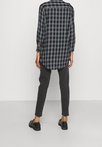 Svartvit rutigt långärmad skjorta med uppkavlade ärmar, ihopparad med mörkgrå smalpassande byxor och svarta skor. Mjuk tygstruktur.