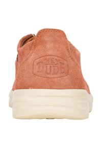 Zapato slip-on de ante coral claro con un acabado texturizado, que presenta una suela crema y el logo "HEY DUDE" grabado en el talón.