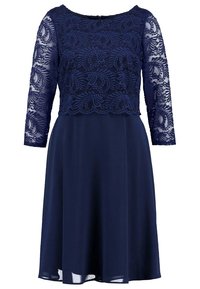 Námořnická modrá šaty s krajkovým korzetem a rukávy po tři čtvrtiny, hladká sukně a kulatý výstřih, s kraječkovým lemem ve tvaru vlnky.