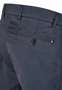 Dunkelblaue Hosen aus leichtem Stoff, mit glatter Textur, standardmäßigen Taschen und einem Knopf-Akzent mit einem kleinen dreifarbigen Patch.