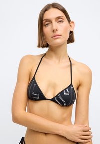 Τριγωνικό μπικίνι τοπ σε μαύρο χρώμα με γυαλιστερό γεωμετρικό σχέδιο. Οι λεπτές ταινίες και ο μινιμαλιστικός σχεδιασμός αναδεικνύου�ν την απαλή υφή του υφάσματος.