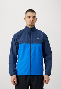 Giacca a vento con zip frontale, caratterizzata da una parte superiore blu navy e una parte inferiore blu brillante, polsini elasticizzati e un logo discreto sul petto.