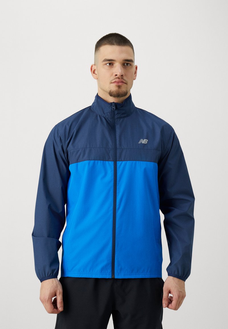Giacca a vento con zip frontale, caratterizzata da una parte superiore blu navy e una parte inferiore blu brillante, polsini elasticizzati e un logo discreto sul petto.