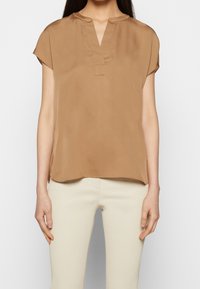 Kurzärmlige Bluse in Hellbraun, hergestellt aus glattem Stoff. Sie verfügt über einen V-Ausschnitt und eine lockere Passform mit einem leicht abgerundeten Saum.