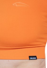 Oranje atletische crop top gemaakt van rekbare stof. Heeft een subtiel logo in reliëf op de borst en een zwart label bij de zoom.