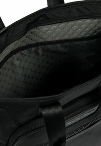 Bolsa textil negra con un interior gris con patrón de panal. Cuenta con resistentes asas negras y un compartimento con cremallera. Diseño simple y funcional.