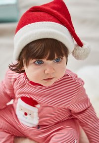 Rood en wit gestreepte babyoutfit met een zakje in de vorm van een kerstman, gecombineerd met een rood-wit gebreide kerstmuts met een pompon.