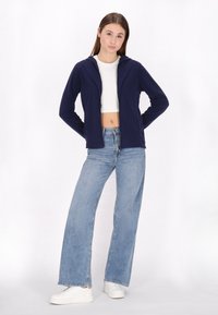 Felpa con zip di colore blu navy con cappuccio, abbinata a jeans a vita alta di un azzurro chiaro a gamba ampia e sneakers bianche. Tessuto dalla consistenza liscia.