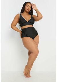 Svart bikini-set i två delar som betonar en bikiniunderdel med hög midja och en mjuk textur. Toppen har en djup V-ringning och vit kantdetalj.