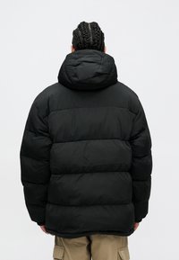 Fekete puffkabát, kapucnival, steppelt mintával és szoros fazonnal. Az anyag fényesnek és szigeteltnek tűnik.