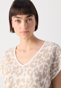 T-shirt à col en V à manches courtes en blanc avec un imprimé léopard doré. Tissu doux avec un subtil éclat et une coupe décontractée. Pas d'autres détails notables.