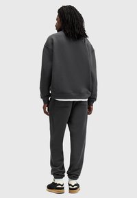 Mørkegrå sweatshirt og matchende bukser i en afslappet pasform, med ribbede manchetter og blød tekstur. Sneakers har sorte og hvide detaljer.