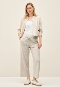 Light beige bomber jacket over a white tank top, paired with vertical striped wide-leg pants in neutral tones and white sneakers.