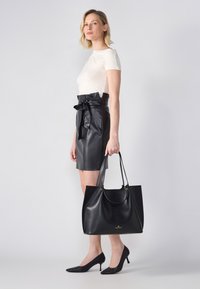 Svart läder tote-väska med en slät yta, två handtag och guldfärgade detaljer. Med en minimalistisk design, perfekt att kombinera med en figurnära vit topp och en svart kjol.