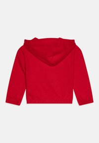Sweatshirt rouge avec une poche avant, des manches longues à poignets élastiques et une capuche avec cordon de serrage. Le matériau semble doux et extensible.