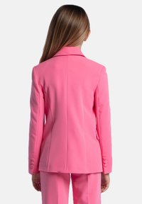 Blazer rosa su misura con colletto a rever, spalle strutturate e polsini abbottonati. Tessuto morbido e design aderente.
