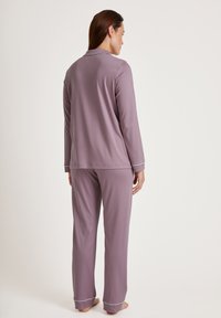 Purple pajama set featuring a long-sleeve top with a collar and contrasting white trim, and matching pants with cuffed hems. Soft fabric.