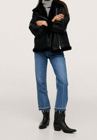 Czarna skórzana kurtka z futrzanym wykończeniem, zapinana na zamek, w połączeniu z prostymi niebieskimi dżinsami i czarnymi botkami na niewielkim obcasie.
