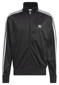 Černá sportovní bunda vyrobená z hladk ého, lehkého materiálu. Obsahuje bílé třípruhové detaily na rukávech a zapínání na zip vpředu. Logo Adidas na hrudi.
