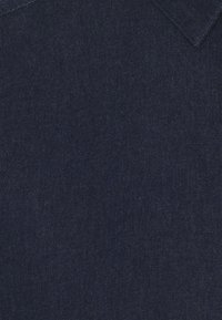 Mörkblå denimtyg med en slät textur och subtilt vävmönster. Har en traditionell kragdesign upptill.