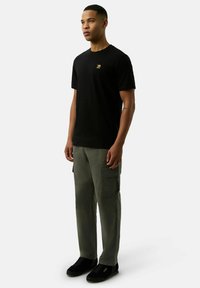 Czarny bawełniany t-shirt z małym złotym logo, połączony z oliwkowymi spodniami cargo z bocznymi kieszeniami oraz czarnymi trampkami z beżowymi podeszwami.