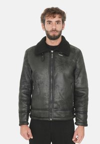 Giacca in ecopelle nera con una finitura testurizzata, dotata di un colletto in peluche nero e tasche laterali con zip. Chiusura con zip sul davanti.