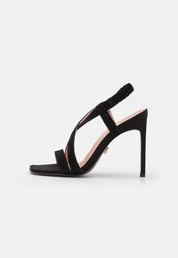 Black suede high-heeled sandal with open toe, crisscross straps, and a gathered ankle strap. Features a sleek silhouette and smooth texture.