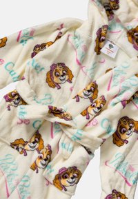 Cream-colored children's bathrobe with pink and blue "Paw Patrol" text and multiple smiling dog character faces printed all over.
