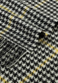 Woven scarf in black, white, and yellow houndstooth pattern with fringe edges, featuring a soft, textured wool blend fabric.