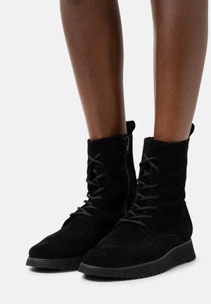 Black suede ankle boots with a textured finish, featuring front laces and a side zipper, supported by a textured rubber sole.